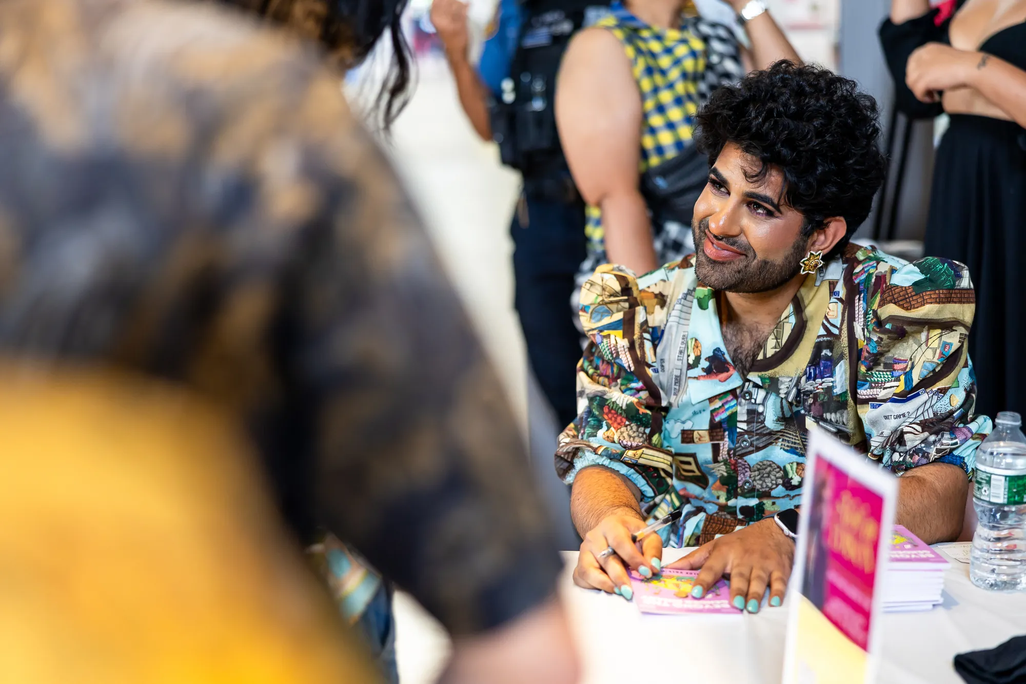 Alok, smiling in a colorful printed shirt, signs books for a line of guests at Desi Rainbow’s community event in Edison, New Jersey.