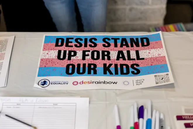 A sign reading Desis Stand Up For All Our Kids on a table next to sign-up sheets.