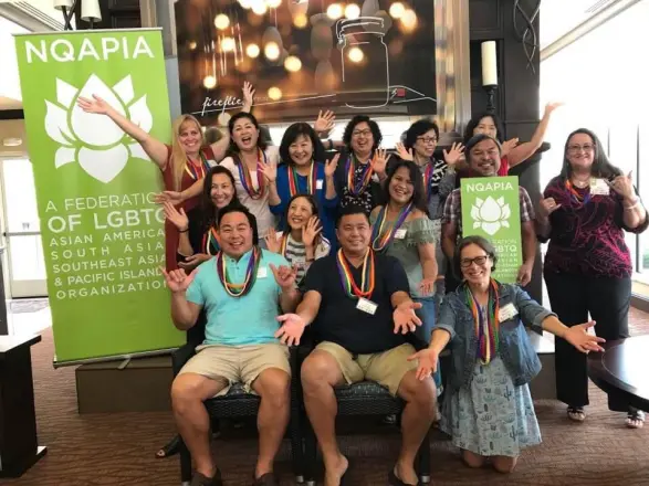 A cheerful group posing in front of an NQAPIA banner at a conference.