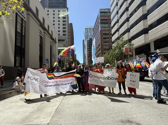 The Desi Rainbow contingent marching with banners between tall city buildings at Pride 2026.