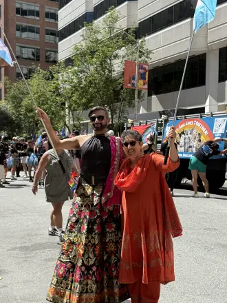 Two marchers in colorful South Asian outfits dancing in the street at Pride 2026.