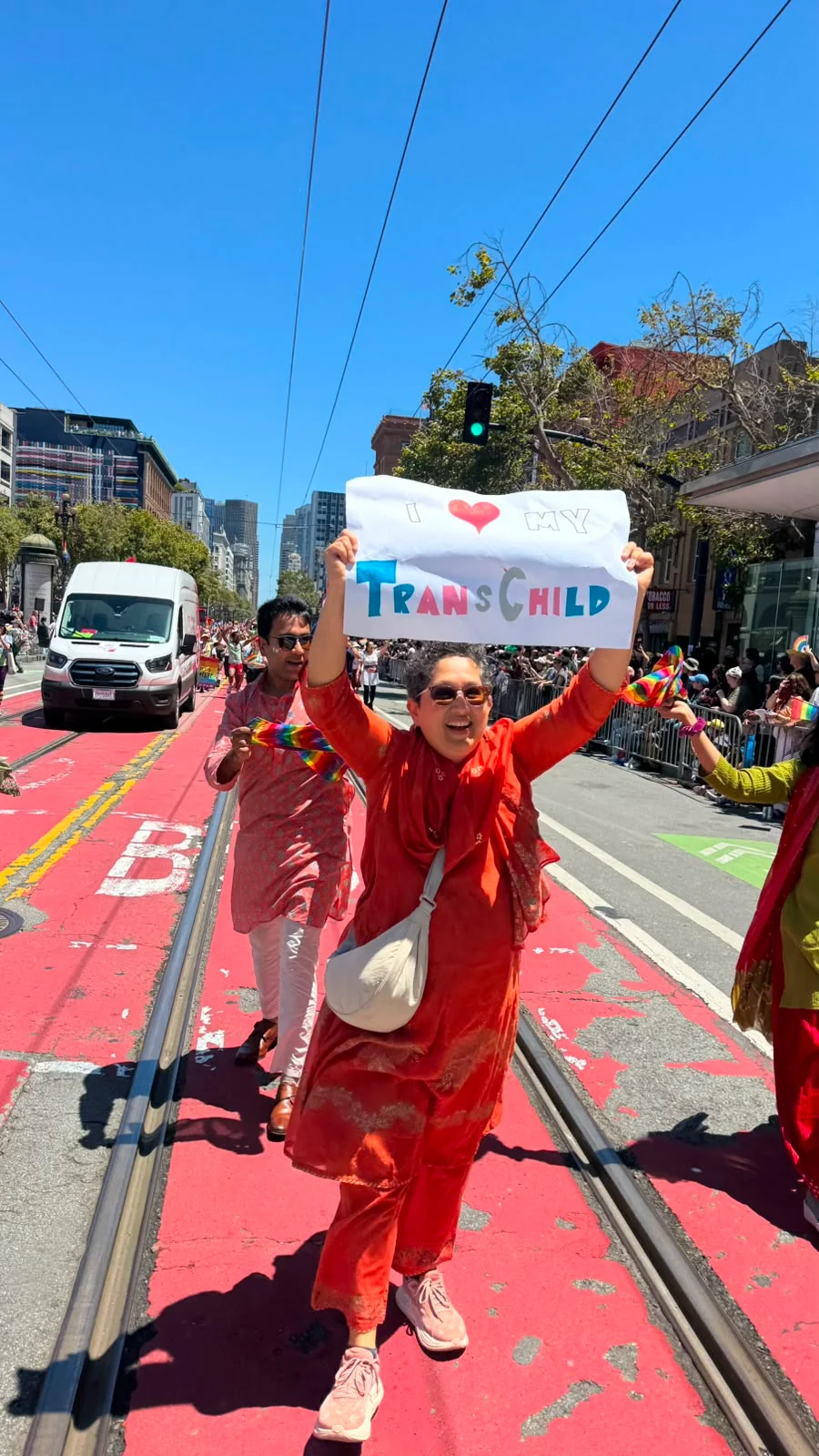 Aruna Rao, Desi Rainbow’s founder, smiling as she marches at Pride with a handmade sign that reads I love my trans child.
