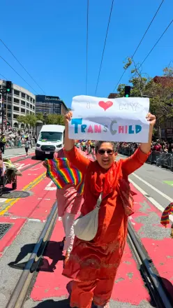 A parent marching at Pride holding a hand-drawn sign with a heart that reads Trans Child.