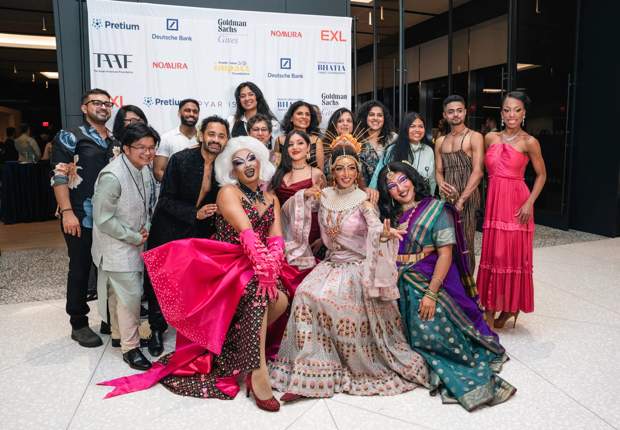 Guests and performers in glittering saris, lehengas and drag looks pose together in front of the sponsor wall at Pyaar is Pyaar, Desi Rainbow’s 2025 fundraiser.