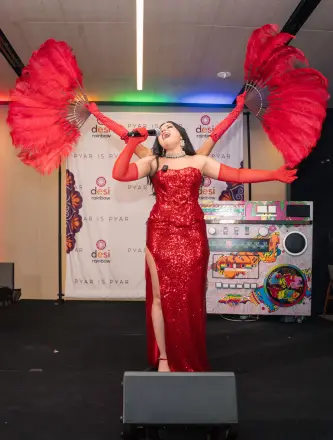 A performer in a red sequined gown singing on stage with red feather fans at Pyar is Pyar.