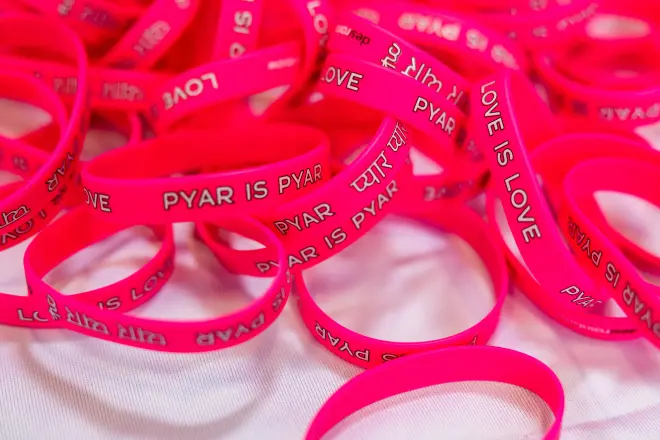 A pile of bright pink wristbands printed with Pyar is Pyar and Love is Love.