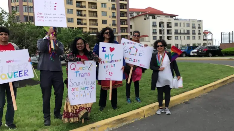 People on a lawn holding hand-made signs about being queer and trans South Asians.