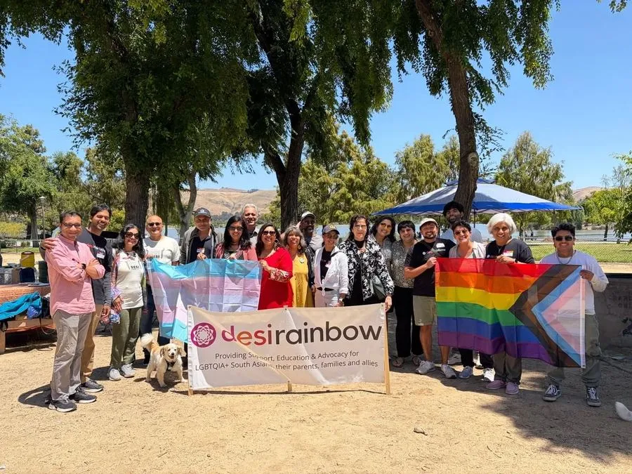 Desi Rainbow members holding the organization's banner alongside rainbow and transgender pride flags at an outdoor gathering.