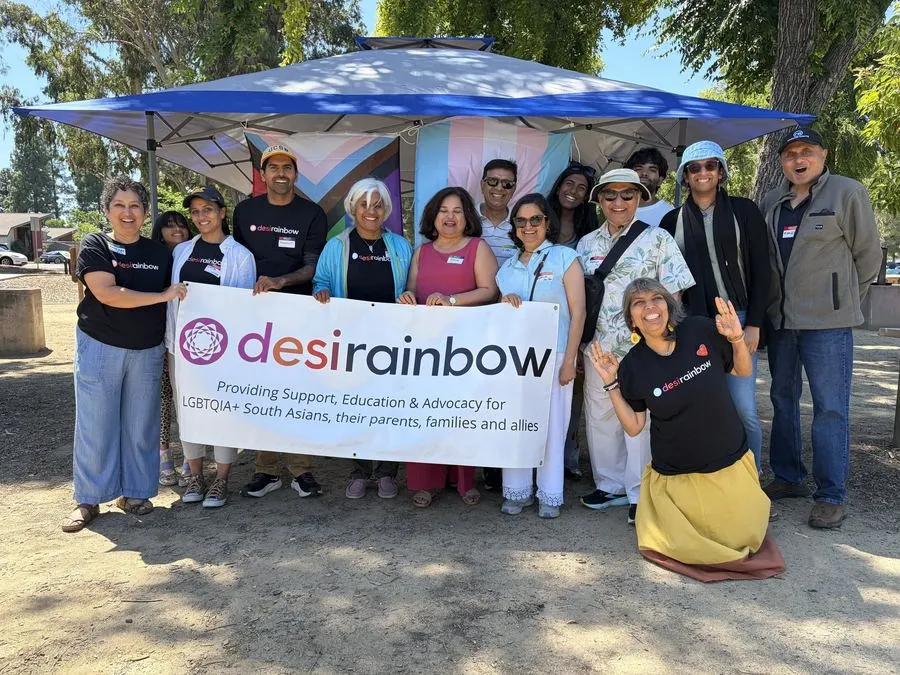 Desi Rainbow members gathered under a canopy behind a banner reading Providing Support, Education and Advocacy for LGBTQIA+ South Asians, their parents, families and allies.